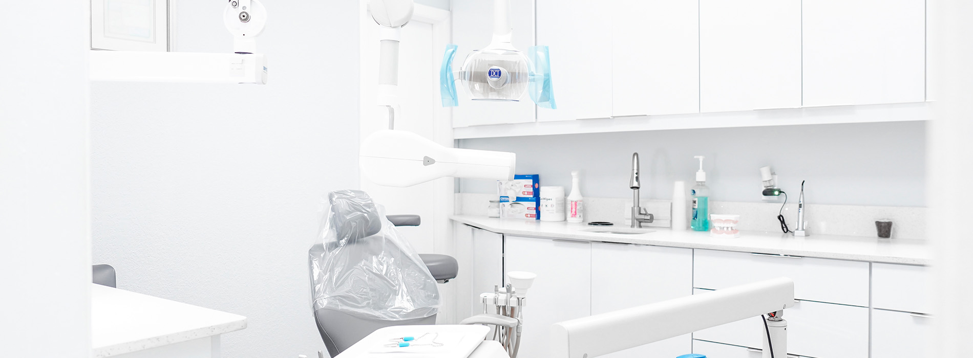The image shows a modern dental clinic interior with various pieces of equipment, including a dental chair and an X-ray machine.