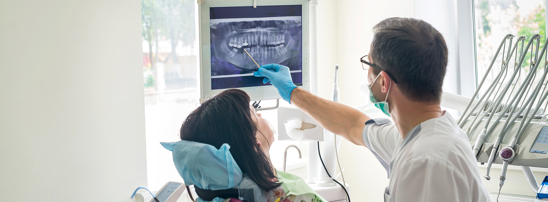 A person is seated in a dental chair, receiving care from a dental professional who stands behind them.