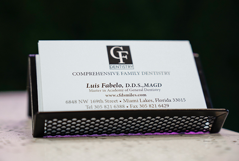 The image shows a business card with text and contact information, placed on a surface with a perforated edge, against a blurred background.