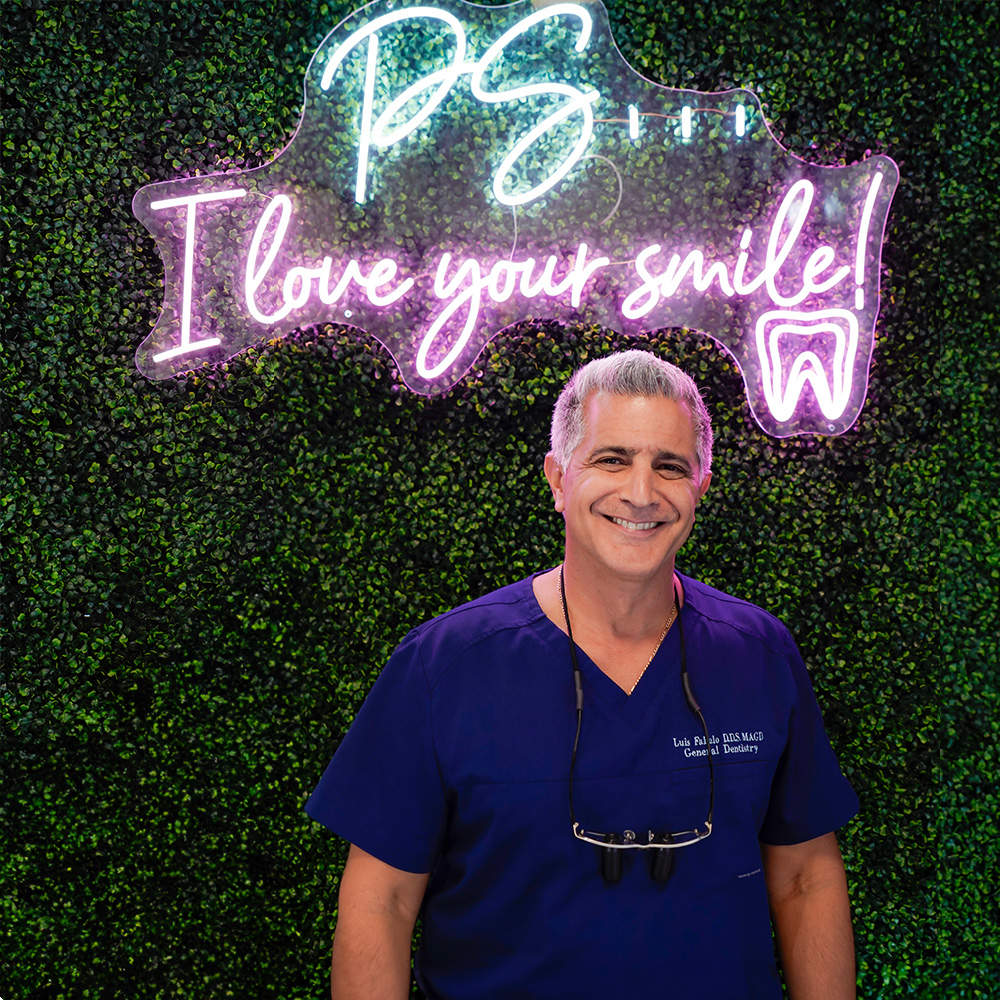 A smiling man wearing a white lab coat stands in front of a sign with the letters  GF  on it.