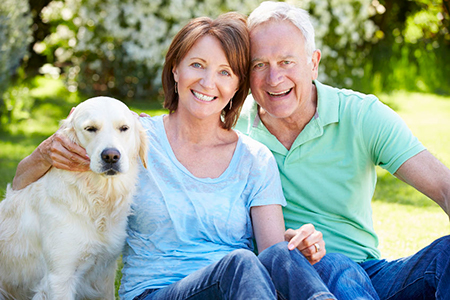 Man and woman posing with a golden retriever dog outdoors.