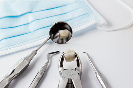 The image shows a dental tool kit with various instruments on a white surface, accompanied by a blue surgical mask.