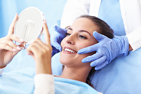 A woman receiving a facial treatment with a magnifying mirror held by a professional, set against a blue background with medical equipment.