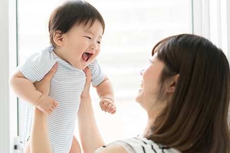 A smiling woman holding a baby with a joyful expression.