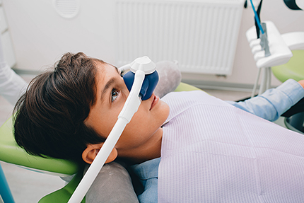 A young boy with a dental device over his face, sitting in a dentist s chair.
